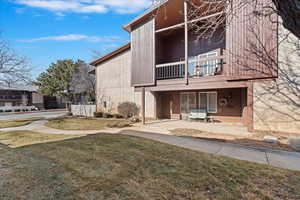 Back of house with a balcony, a patio area, and a lawn