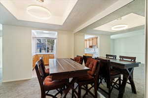 Dining area with a raised ceiling, sink, light carpet, and a textured ceiling