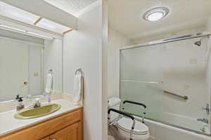 Full bathroom with enclosed tub / shower combo, vanity, a textured ceiling, and toilet