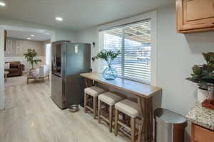 Kitchen with a kitchen bar, stainless steel fridge, and light wood-type flooring