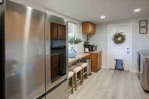 Kitchen with washing machine and clothes dryer, stainless steel fridge, and light hardwood / wood-style flooring