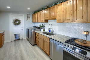 Kitchen featuring sink, stainless steel appliances, light stone countertops, washer and clothes dryer, and light hardwood / wood-style flooring