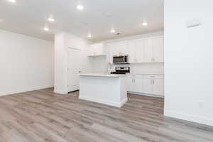 Kitchen with sink, light hardwood / wood-style flooring, appliances with stainless steel finishes, white cabinetry, and a center island with sink