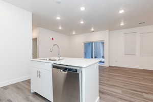 Kitchen featuring white cabinetry, sink, a kitchen island with sink, stainless steel dishwasher, and light wood-type flooring