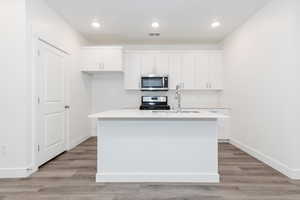 Kitchen featuring sink, stainless steel appliances, an island with sink, and white cabinets