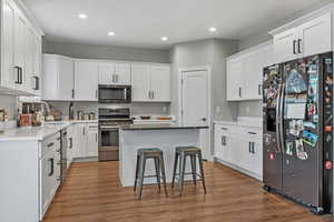 Kitchen with stainless steel appliances, a center island, hardwood / wood-style floors, and white cabinets