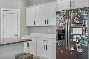 Kitchen featuring stainless steel fridge with ice dispenser, dark stone counters, and white cabinets