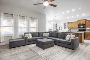 Living room with vaulted ceiling, ceiling fan with notable chandelier, and light wood-type flooring