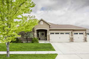 View of front facade with a garage, stucco siding, concrete driveway, stone siding, and a front yard