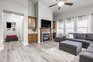 Living room with a high ceiling, a stone fireplace, ceiling fan, and light hardwood / wood-style flooring