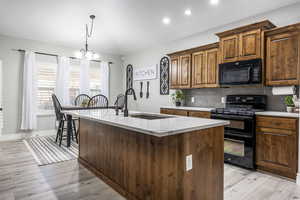 Kitchen featuring sink, a kitchen island with sink, light stone counters, tasteful backsplash, and black appliances