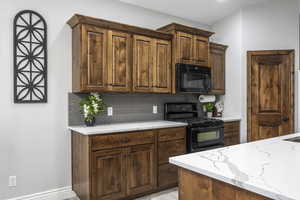 Kitchen with backsplash, black appliances, and light stone countertops