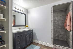 Bathroom with wood-type flooring, a tile shower, vanity, and a textured ceiling