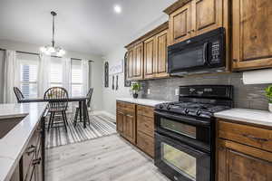 Kitchen with backsplash, light stone countertops, light hardwood / wood-style floors, and black appliances