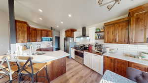 Kitchen with lofted ceiling, wall chimney range hood, sink, light hardwood / wood-style flooring, and appliances with stainless steel finishes