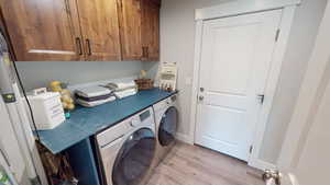 Clothes washing area featuring light hardwood / wood-style floors, cabinets, and washing machine and clothes dryer