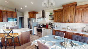 Kitchen featuring lofted ceiling, a breakfast bar, light wood-type flooring, stainless steel appliances, and wall chimney range hood