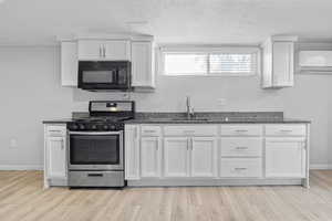 Basement Kitchen with sink, granite countertops,  white cabinets, and gas stove.