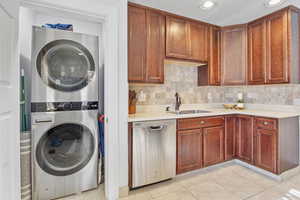 Kitchen  and laundry with stainless steel dishwasher, stacked washer / drying machine, sink, and backsplash