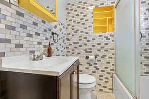 Full bathroom with vanity, combined bath / shower with glass door, tile walls, and toilet