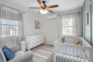 Bedroom featuring light carpet, a crib, an AC wall unit, and ceiling fan