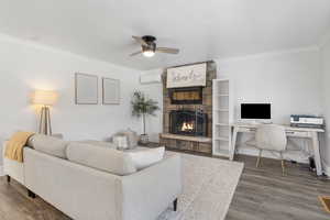 Living room with crown molding, ceiling fan, a wall mounted air conditioner, a fireplace, and laminate / wood-style flooring