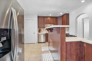 Kitchen featuring appliances with stainless steel finishes, a breakfast bar, tasteful backsplash, light tile patterned floors, and kitchen peninsula