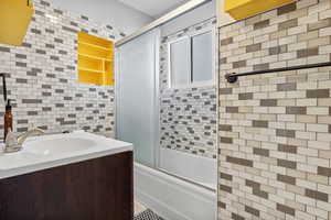 Bathroom featuring enclosed tub / shower combo, tile walls, vanity, and decorative backsplash