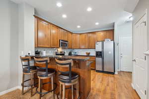 Kitchen with a breakfast bar area, stainless steel appliances, light hardwood / wood-style floors, Granite countertops.