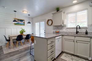 Kitchen with white dishwasher, sink, light stone counters, and kitchen peninsula