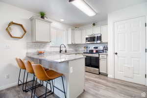 Kitchen featuring appliances with stainless steel finishes, white cabinetry, sink, a kitchen bar, and kitchen peninsula