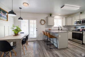 Kitchen featuring decorative light fixtures, a breakfast bar area, white cabinets, and appliances with stainless steel finishes