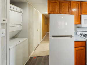 Kitchen with white appliances, dark hardwood / wood-style flooring, and stacked washer and dryer