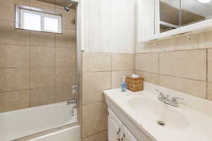 Bathroom with tiled shower / bath, vanity, and tile walls