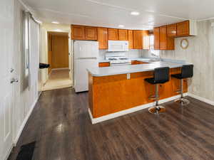 Kitchen with sink, white appliances, a wall mounted air conditioner, dark hardwood / wood-style flooring, and kitchen peninsula