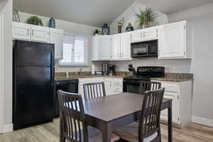 Kitchen with white cabinetry, light wood-type flooring, black appliances, and lofted ceiling