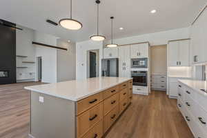 Kitchen with appliances with stainless steel finishes, a spacious island, white cabinets, hanging light fixtures, and light hardwood / wood-style flooring