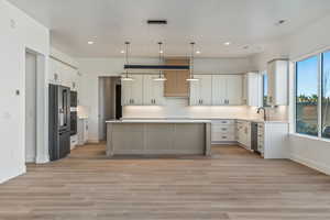 Kitchen featuring white cabinetry, light hardwood / wood-style flooring, a kitchen island, pendant lighting, and stainless steel appliances