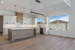 Kitchen with hanging light fixtures, dishwasher, white cabinets, and a kitchen island