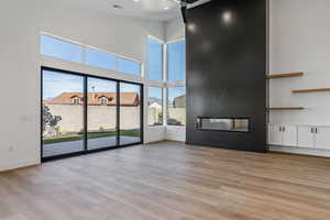 Unfurnished living room featuring a towering ceiling, a large fireplace, and light hardwood / wood-style flooring