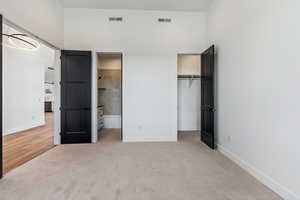 Unfurnished bedroom featuring a walk in closet, ensuite bath, a closet, and carpet