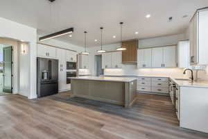 Kitchen with high quality fridge, built in microwave, white cabinets, hanging light fixtures, and a center island