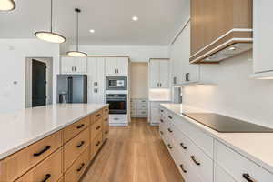 Kitchen with premium range hood, pendant lighting, stainless steel appliances, light hardwood / wood-style floors, and white cabinets