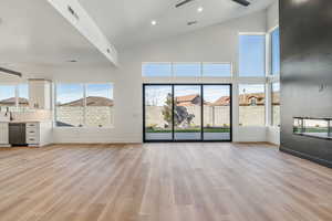 Unfurnished living room featuring ceiling fan, high vaulted ceiling, and light wood-type flooring