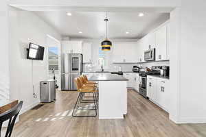 Kitchen with hanging light fixtures, a kitchen island, white cabinets, and appliances with stainless steel finishes