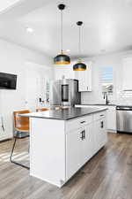 Kitchen with hardwood / wood-style flooring, stainless steel appliances, decorative light fixtures, and white cabinets