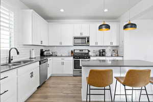 Kitchen featuring sink, appliances with stainless steel finishes, white cabinetry, a kitchen bar, and decorative light fixtures