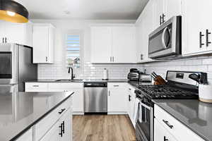 Kitchen featuring appliances with stainless steel finishes, sink, white cabinets, dark stone counters, and light hardwood / wood-style flooring