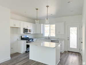 Kitchen featuring appliances with stainless steel finishes, decorative light fixtures, a kitchen island, and white cabinets