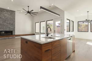 Kitchen featuring a stone fireplace, dishwasher, sink, light wood-type flooring, and a spacious island